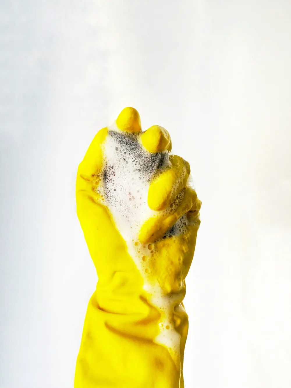 Yellow rubber glove holding a soapy sponge